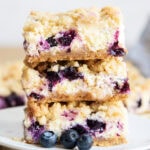 A stack of three pieces of Blueberry Lemon Cheesecake Bars on a plate with crumb topping.