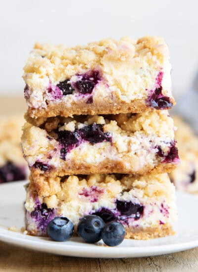 A stack of three pieces of Blueberry Lemon Cheesecake Bars on a plate with crumb topping.