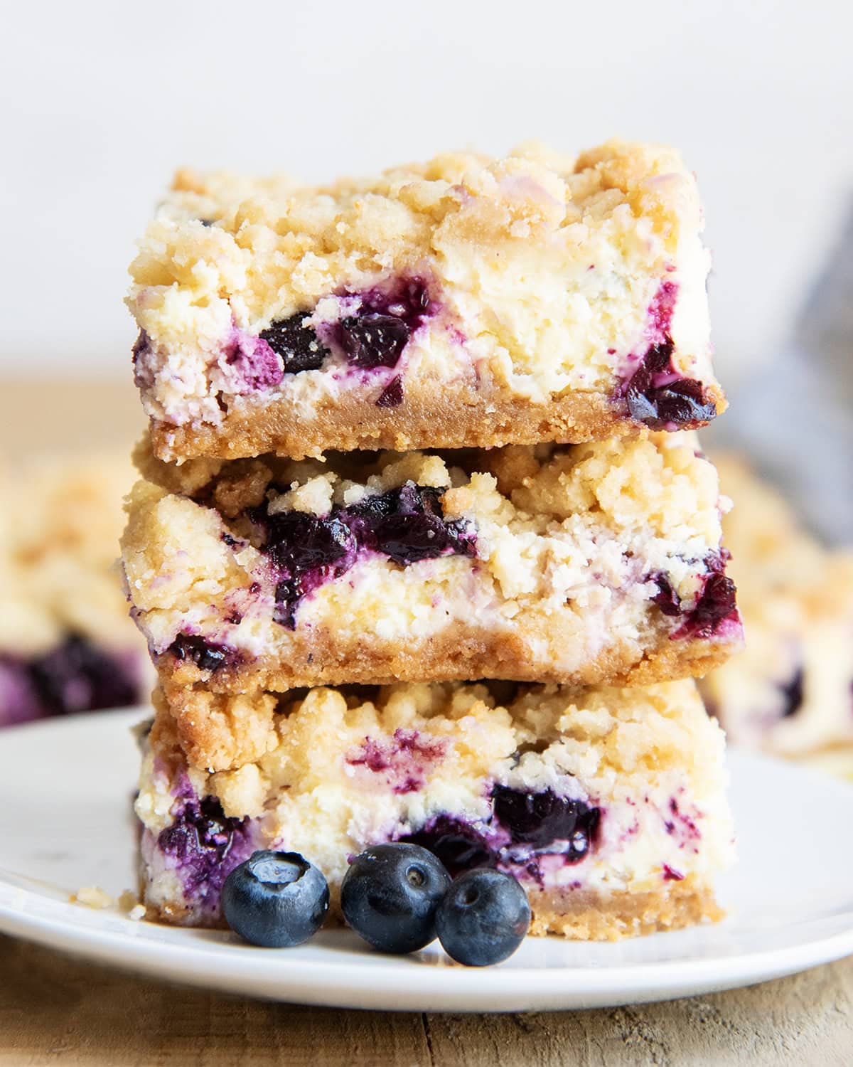 A stack of three pieces of Blueberry Lemon Cheesecake Bars on a plate with crumb topping.