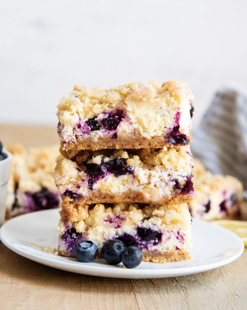 A stack of three pieces of Blueberry Lemon Cheesecake Bars on a plate with crumb topping.