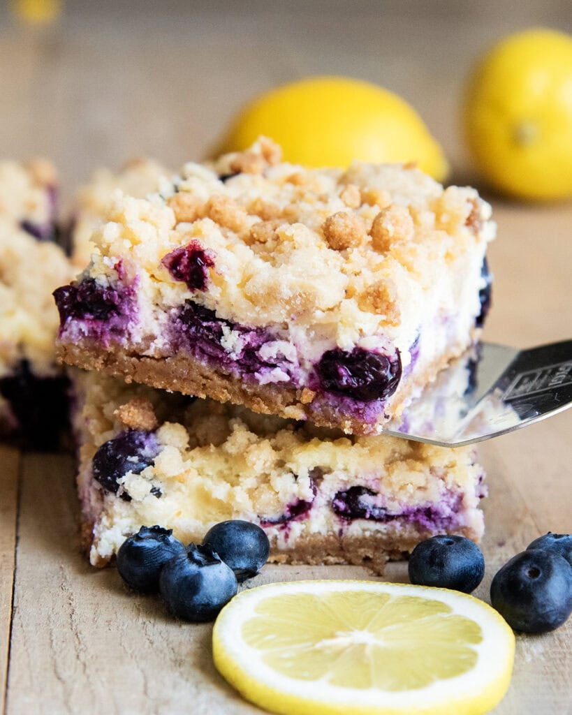 A stack of two blueberry lemon cheesecake bars, and one has a spatula under it. 