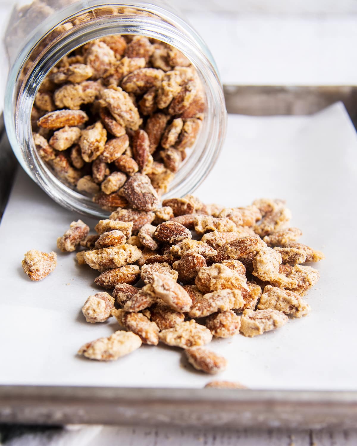 A jar pouring candied almonds onto a baking pan.