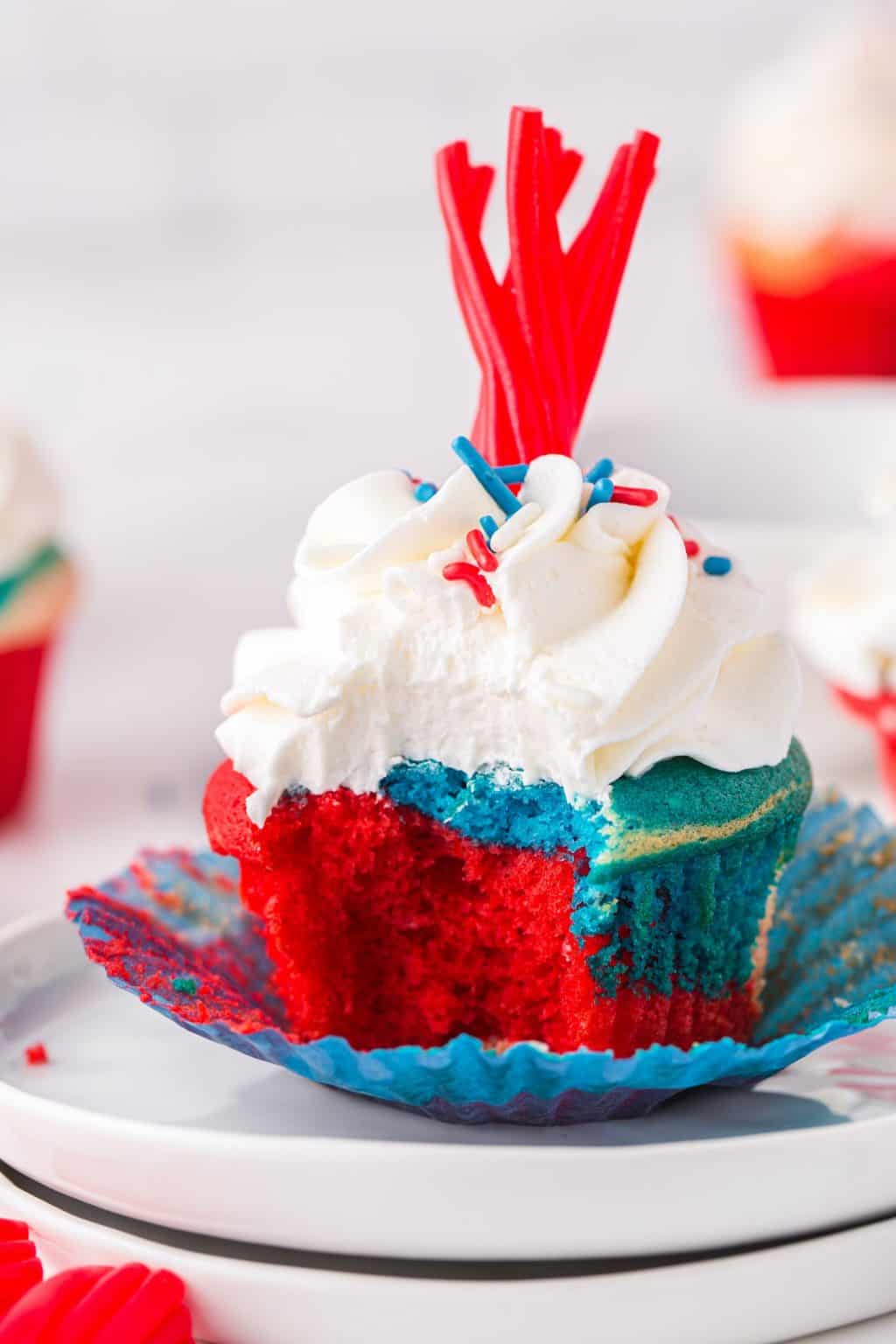 A red, and blue cupcake topped with white frosting, and a red twizzler. 