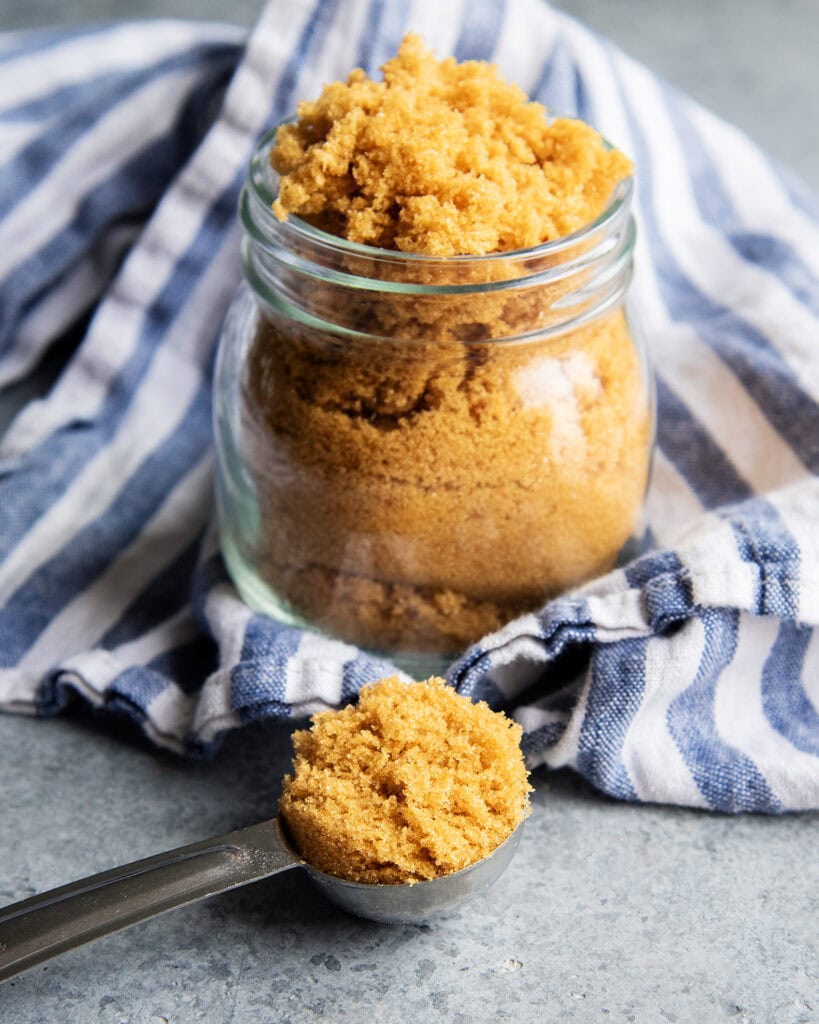 A Tablespoon measuring spoon full of brown sugar in front of a jar of it.