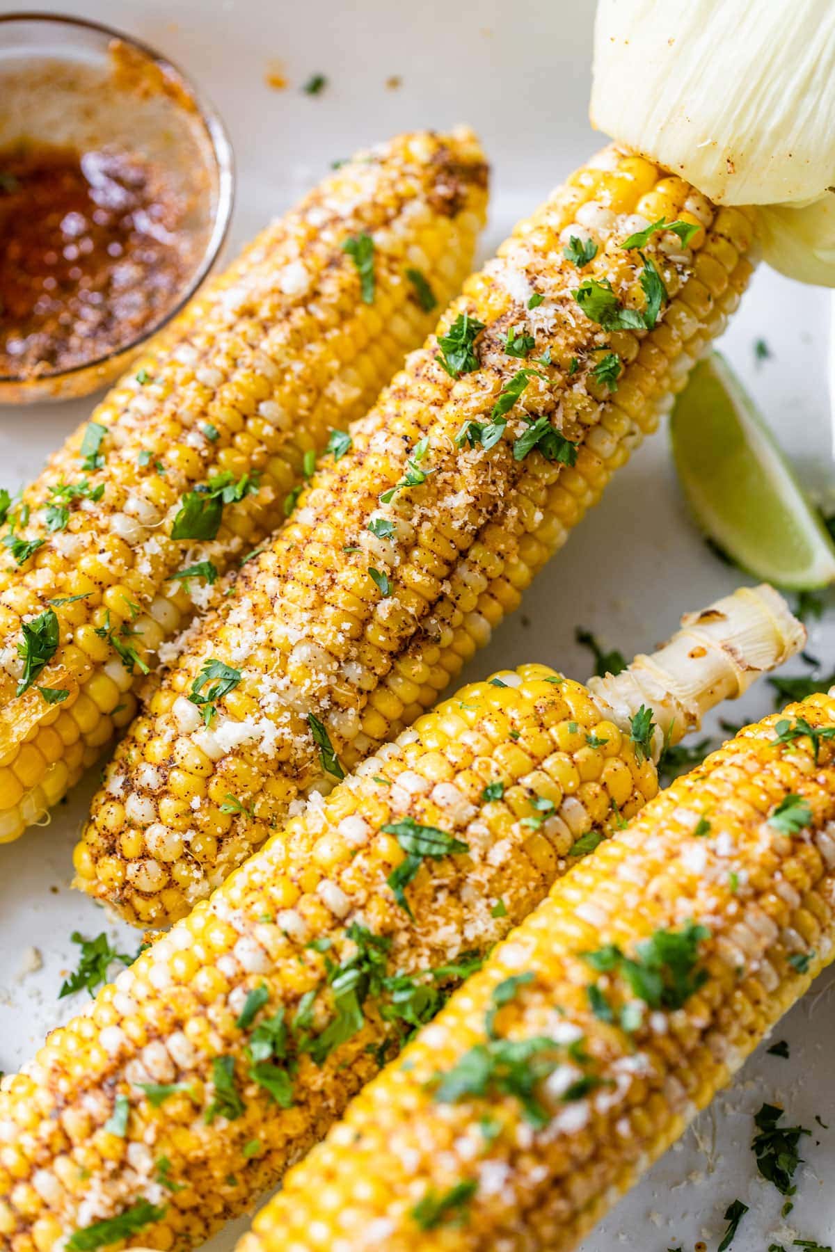 Four ears of corn topped with spices, cilantro, and cheese. 