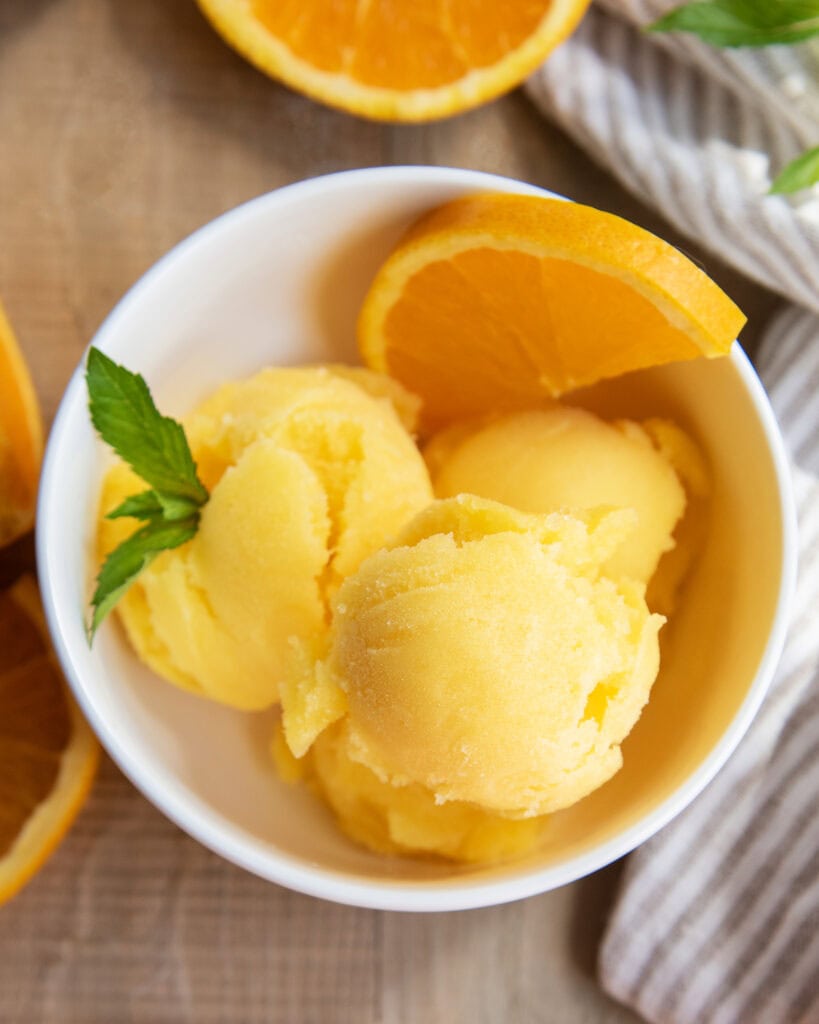 An above view of a bowl of orange sorbet with a mint sprig on it.