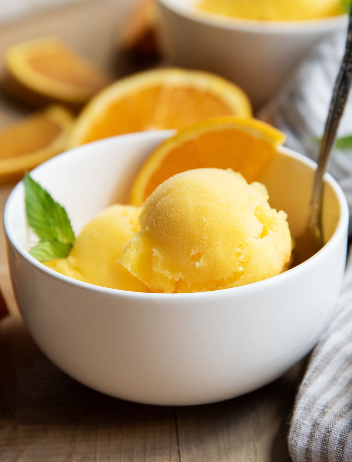 A bowl of scoops of orange sorbet with an orange slice and a mint leaf.
