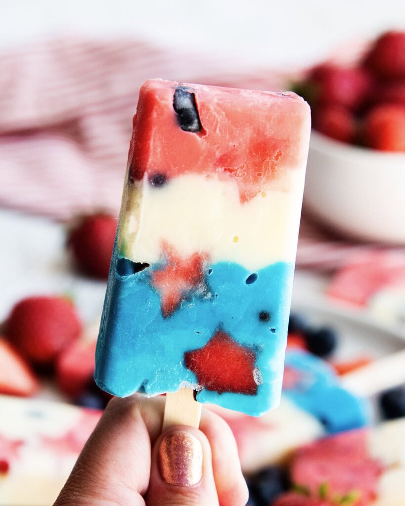 A hand holding a popsicle that is striped red, white, and blue with star shaped strawberries in it.