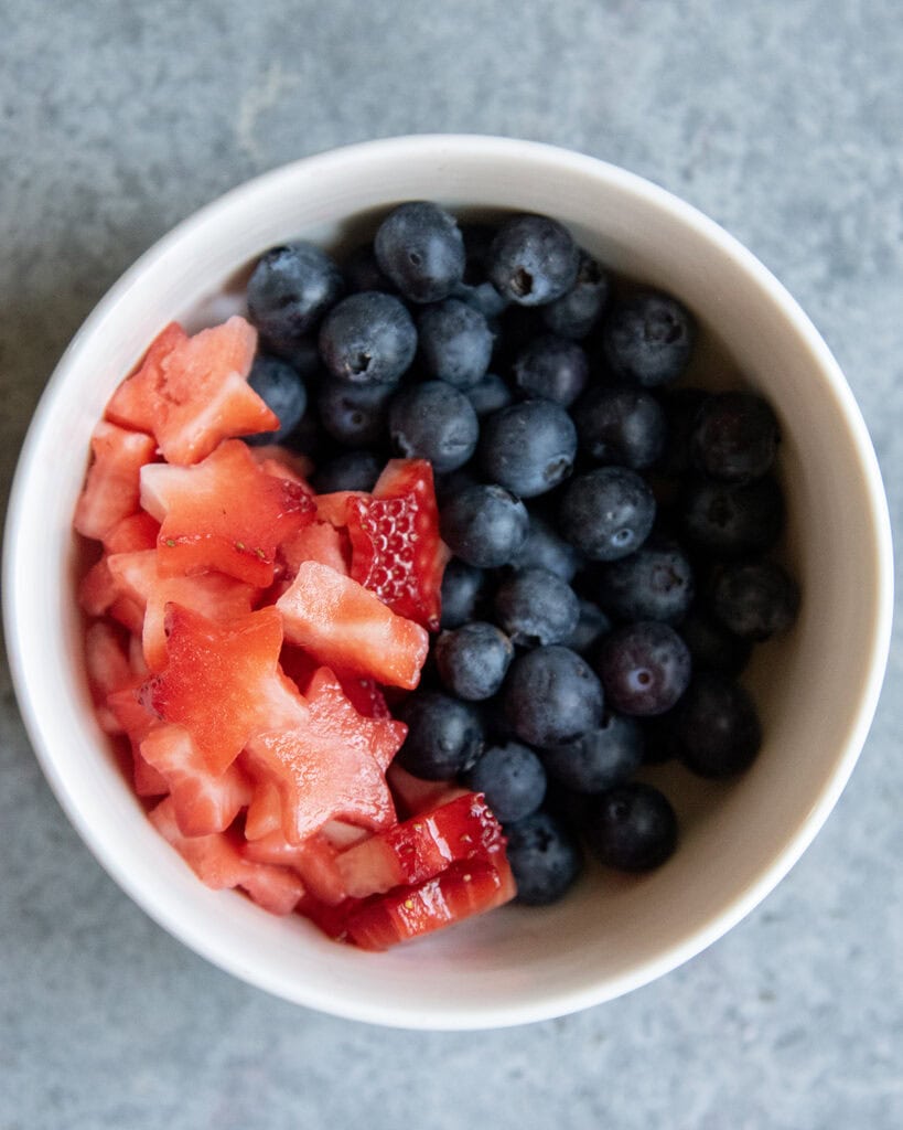 A bowl of star shaped strawberry pieces and blueberries. 