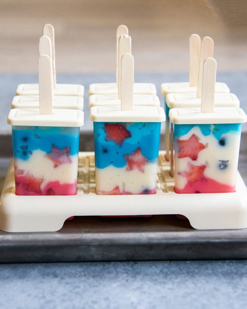 Popsicles in a popsicle stand with their plastic containers on.