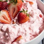 A close up of a bowl of strawberry fluff topped with fresh strawberries.