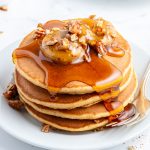 A stack of sweet potato pancakes on a plate topped with pecan butter and syrup.