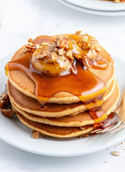A stack of sweet potato pancakes on a plate topped with pecan butter and syrup.