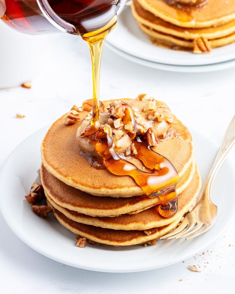 Syrup being poured on a stack of sweet potato pancakes.