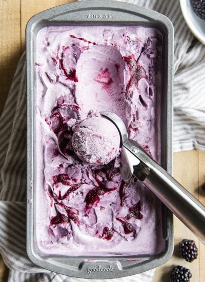 An overhead photo of a purple blackberry ice cream in a metal pan with one scoop in a ball in an ice cream scoop.