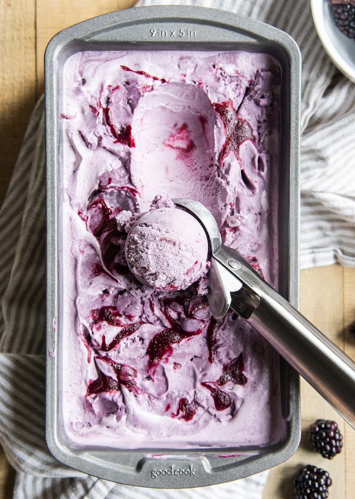 An overhead photo of a purple blackberry ice cream in a metal pan with one scoop in a ball in an ice cream scoop.