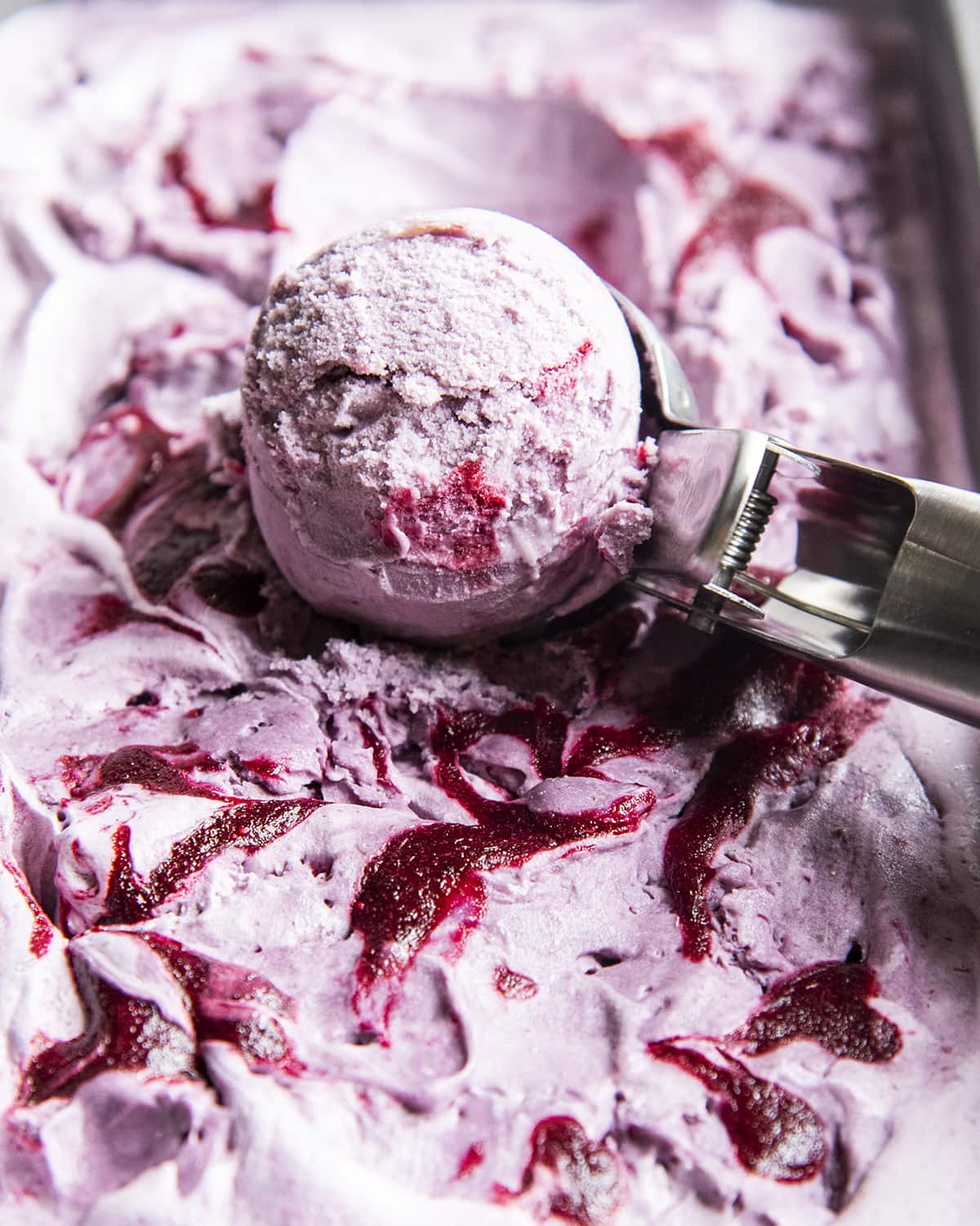 A close up of a scoop of purple blackberry ice cream in an ice cream scooper.