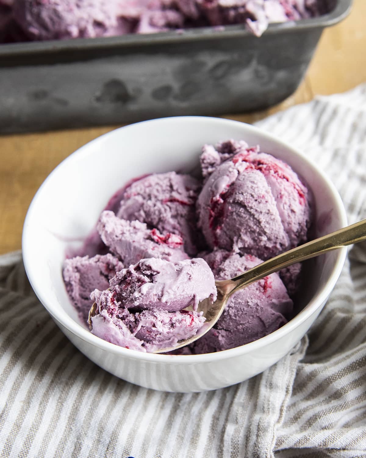 A bowl of purple blackberry ice cream with swirls of berries, and a spoonful of ice cream in a golden spoon.