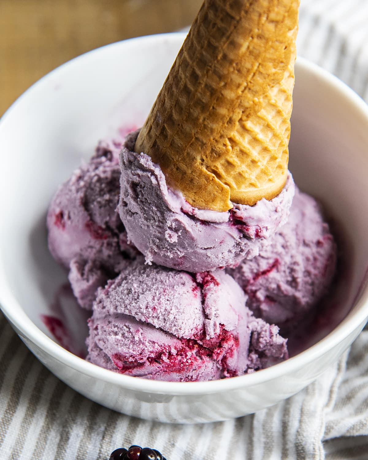Blackberry ice cream in a bowl topped with an upside down ice cream cone.
