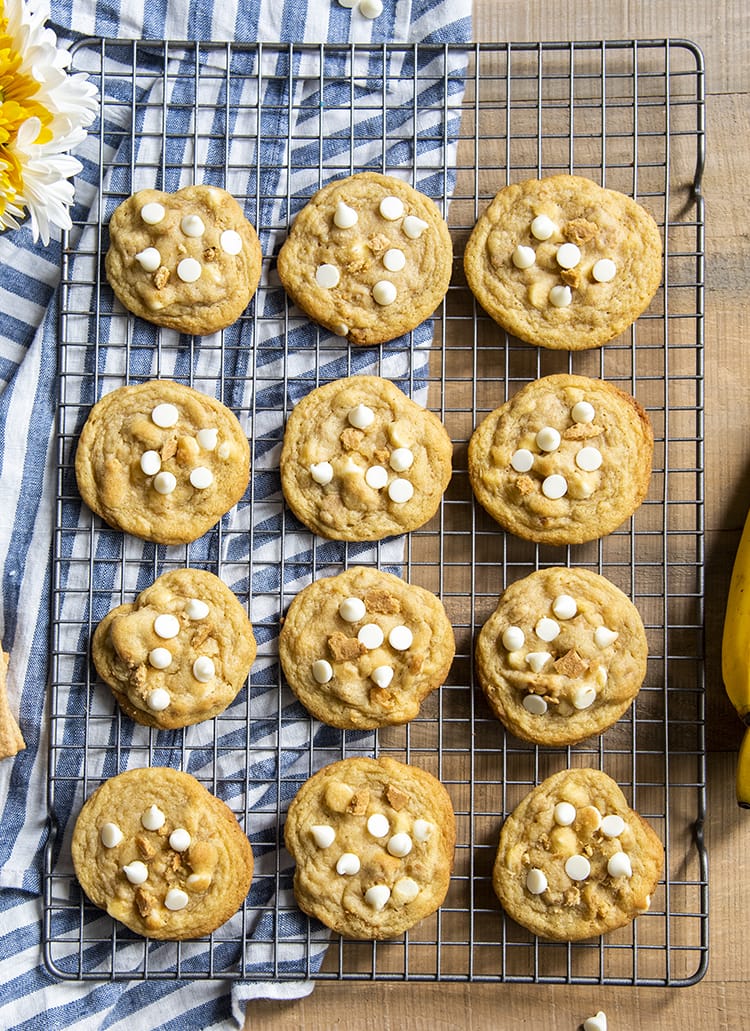 Banana cream pie cookies on a cooling rack topped with graham cracker pieces and white chocolate chips.