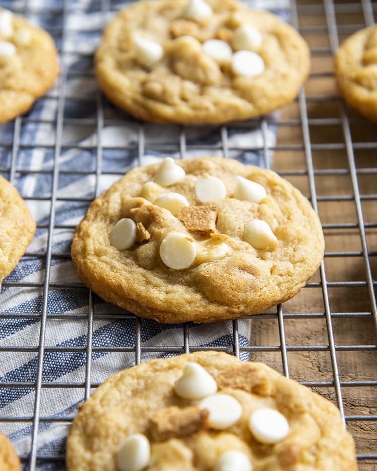A close up of a cookie on a cooling rack. The cookie has white chocolate chips and graham cracker pieces in it.