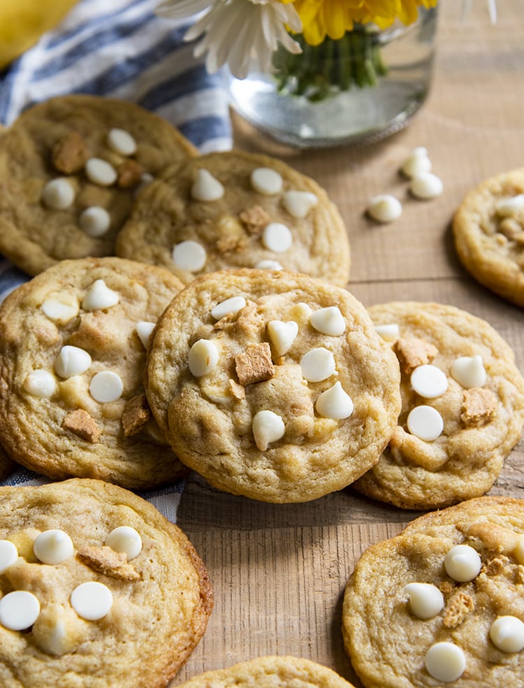 A pile of cookies randomly set on each other. The cookies have white chocolate chips and graham crackers on top of them.