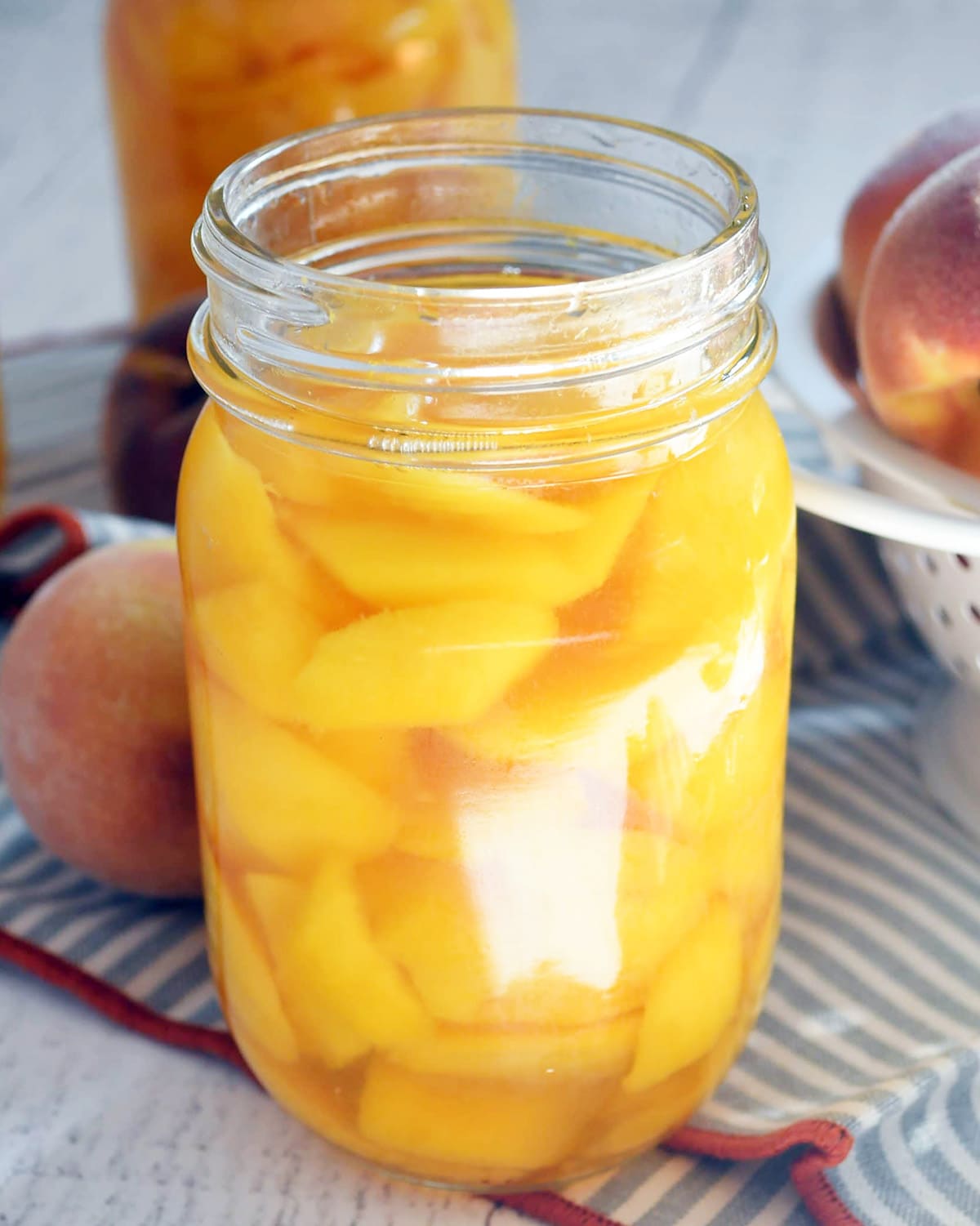 A jar of bottled peaches with the lid off.