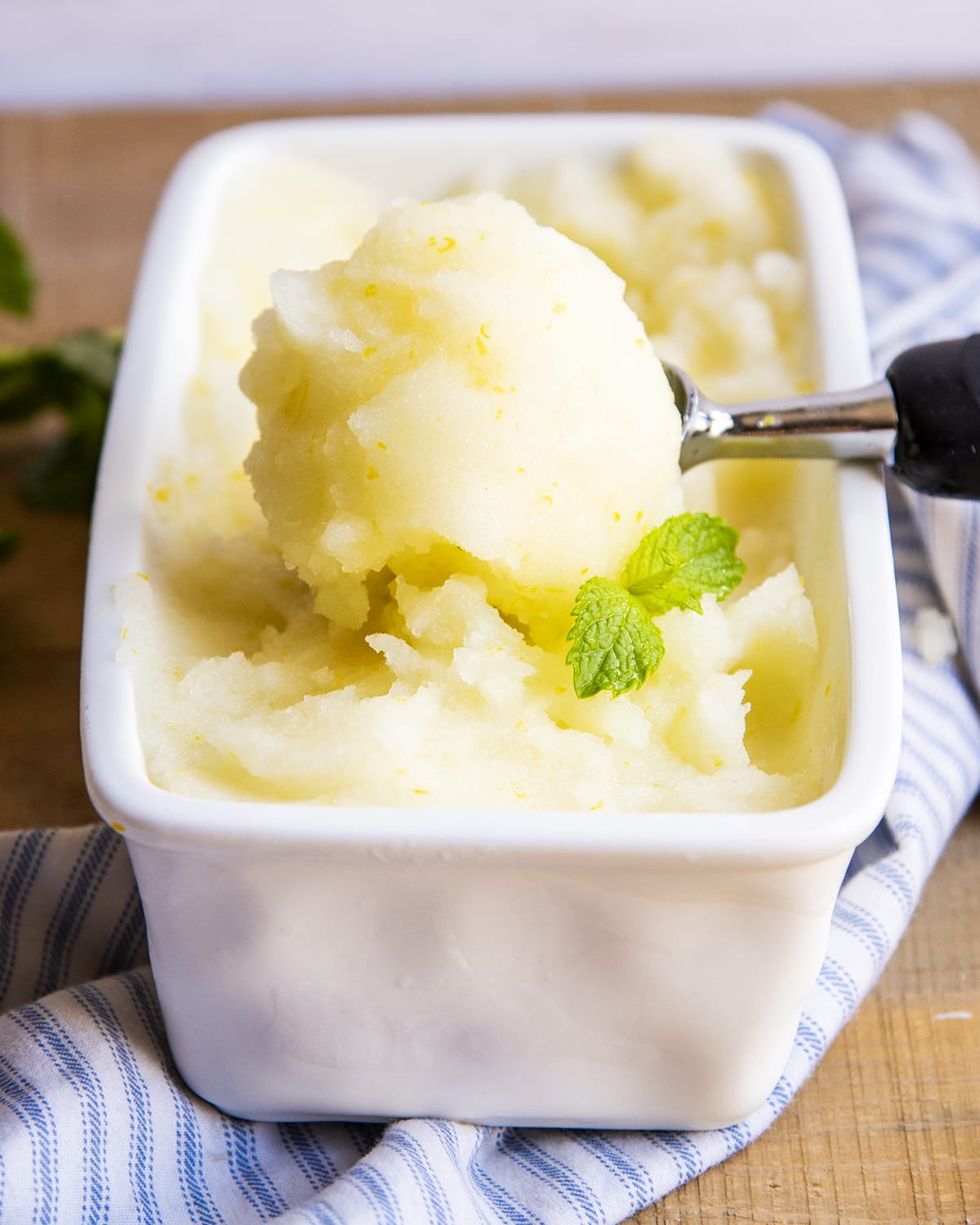 A large scoop of lemon sorbet with a mint leaf in front of it in a container.