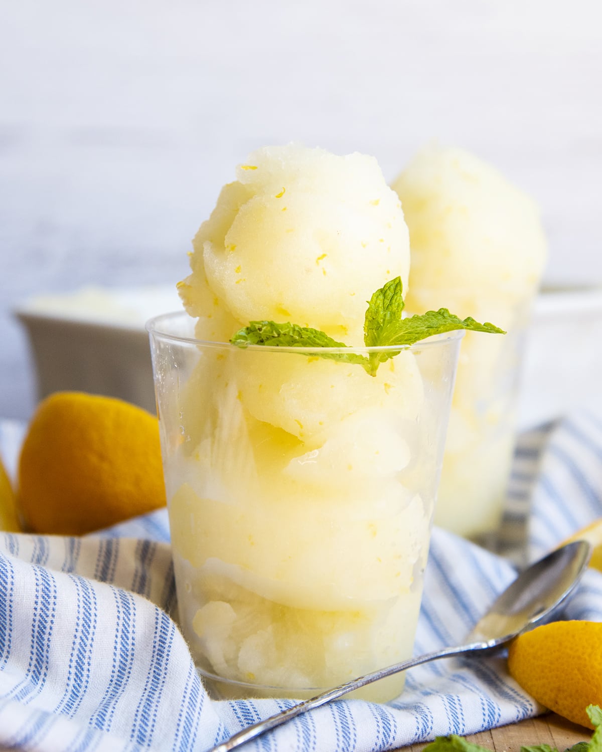 A clear cup full of three scoops of lemon sorbet topped with a mint leaf.