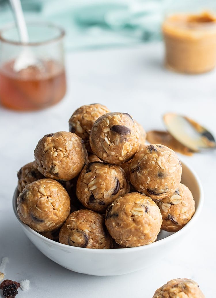A bowl of granola balls, that are made of peanut butter, honey, oats, chocolate chips, coconut, and raisins.