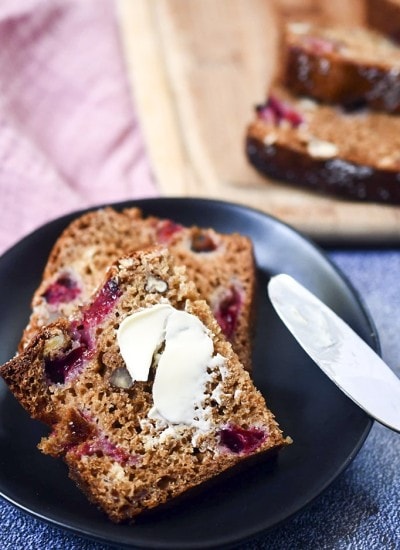 A slice of plum bread with butter spread on top on a black plate.