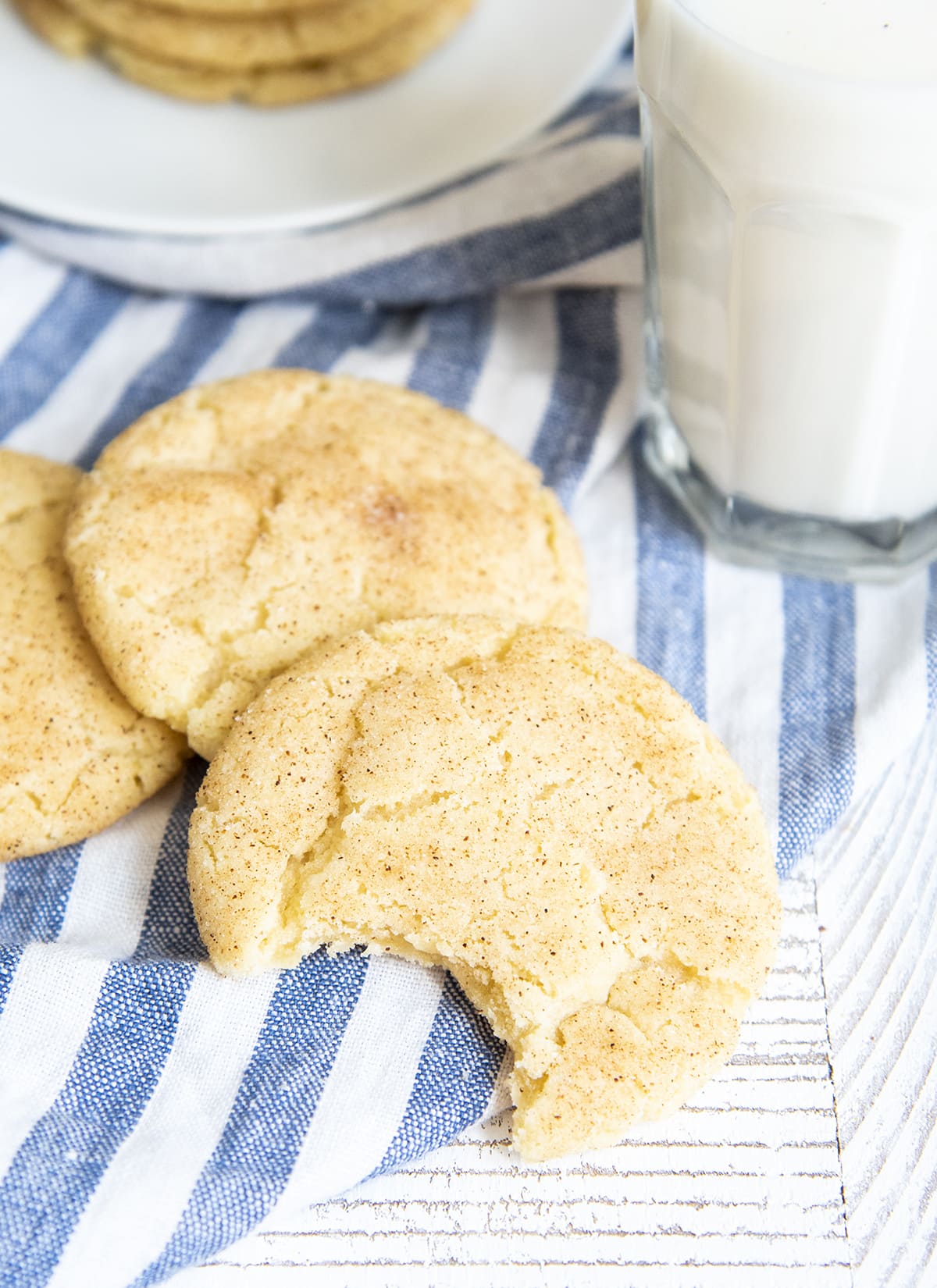 Snickerdoodle cookies on a blue and white cloth, one cookie has a bite out of it.