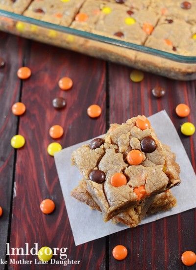 Angled view of reeses pieces peanut butter blondies on a white parchment.