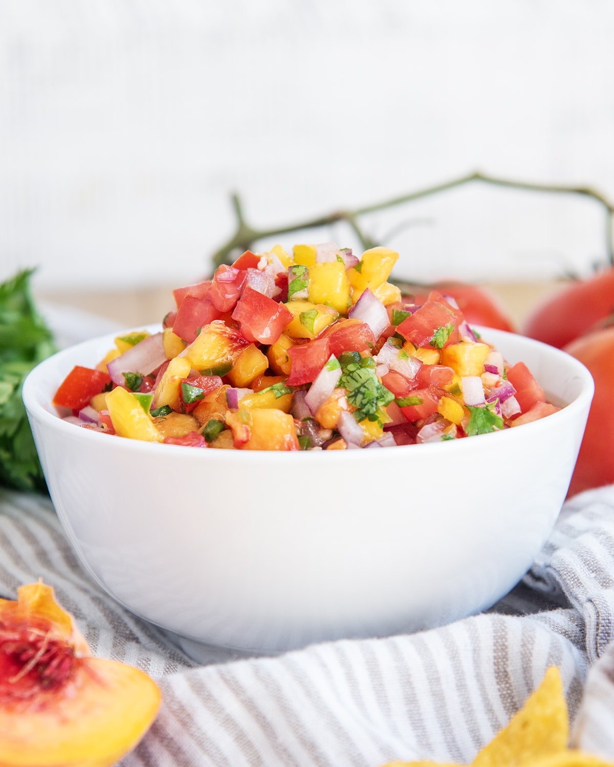 A bowl of peach salsa with tomatoes, red onion, and cilantro.