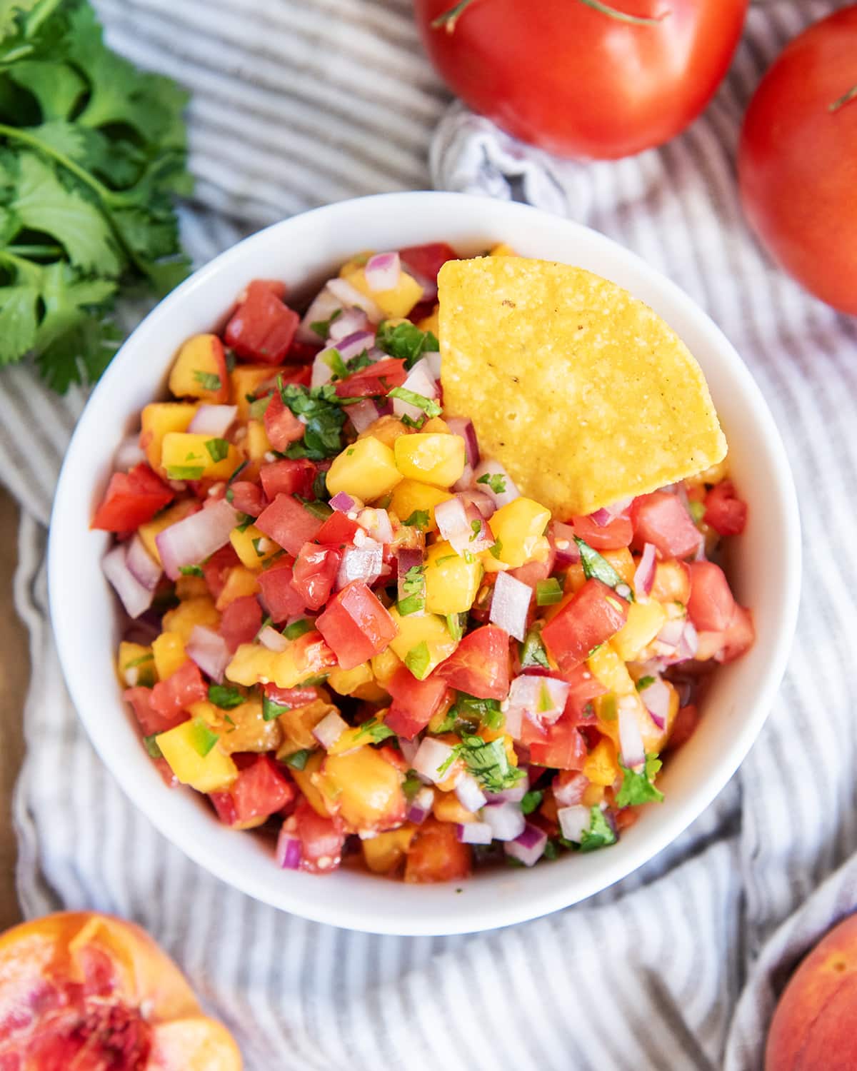 An overhead photo of a bowl of peach and tomato salsa with a tortilla chip in it.
