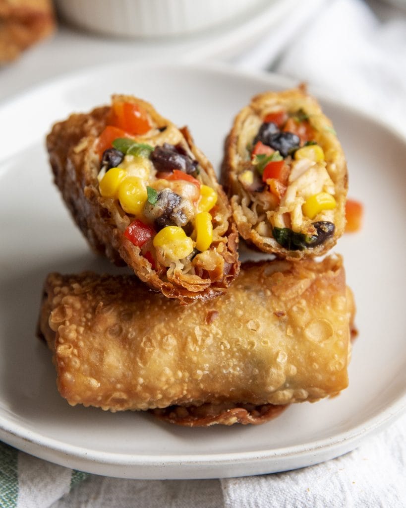 A plate of a southwest chicken egg roll with two cut open halves of another on top.
