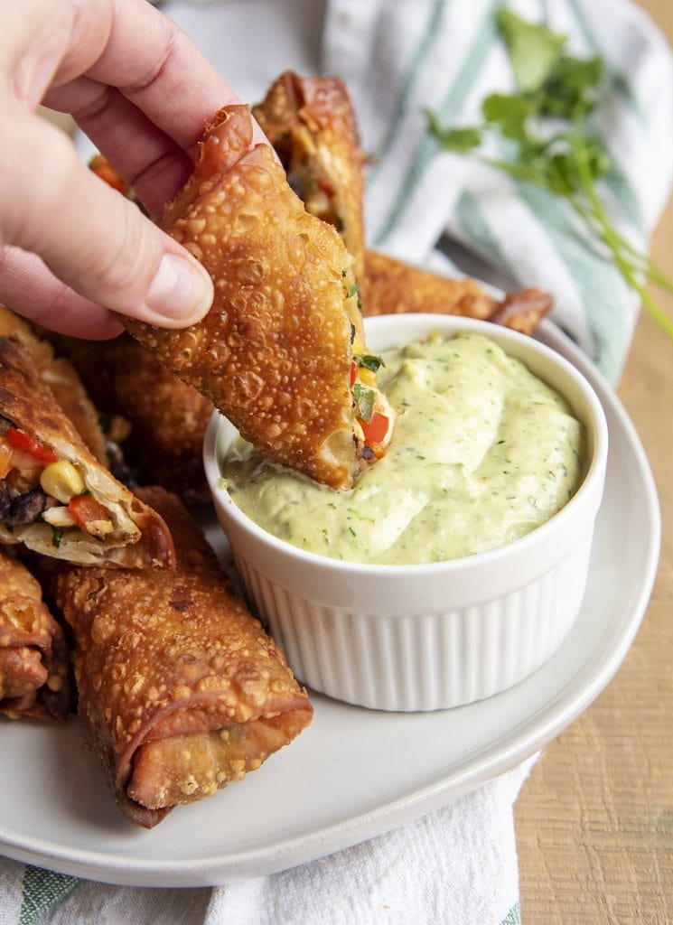 A southwest egg roll dipping into a bowl of avocado ranch dressing.