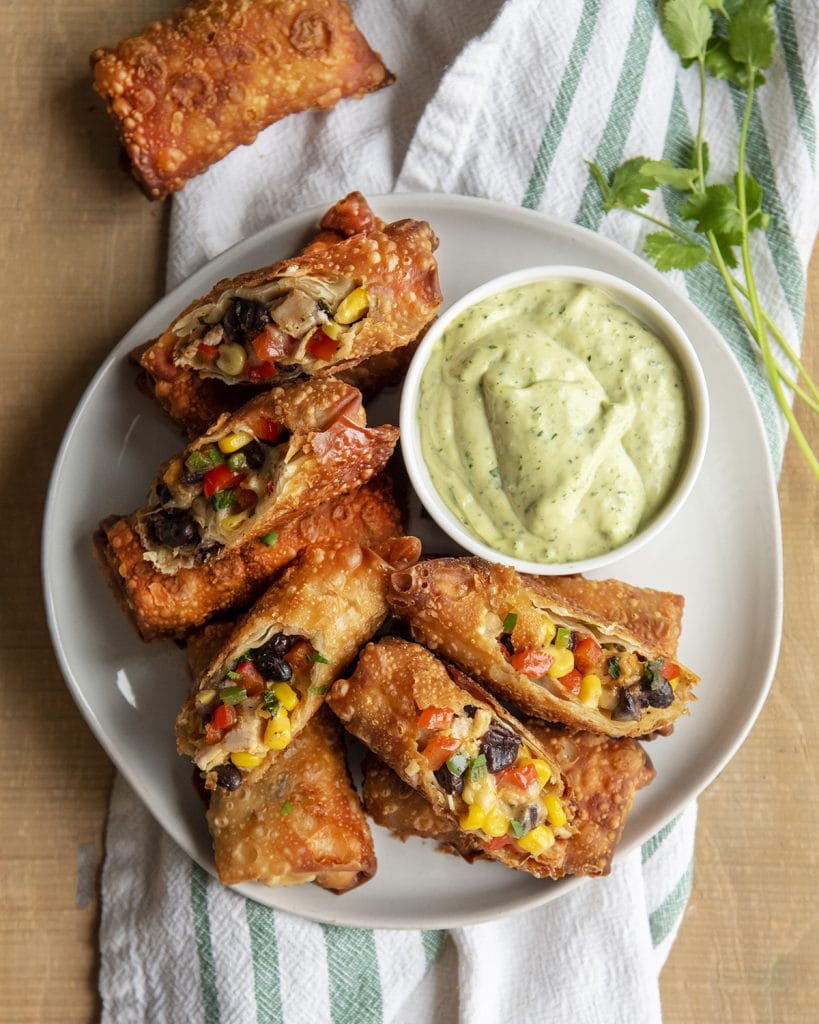 An overhead photo of a plate of southwest chicken rolls with a bowl of avocado ranch dressing.