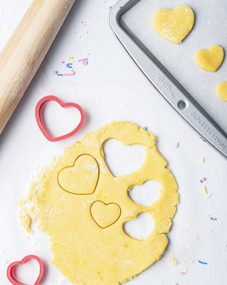Above shot of sugar cookies for two dough being cut out with a heart shaped cookie cutter.