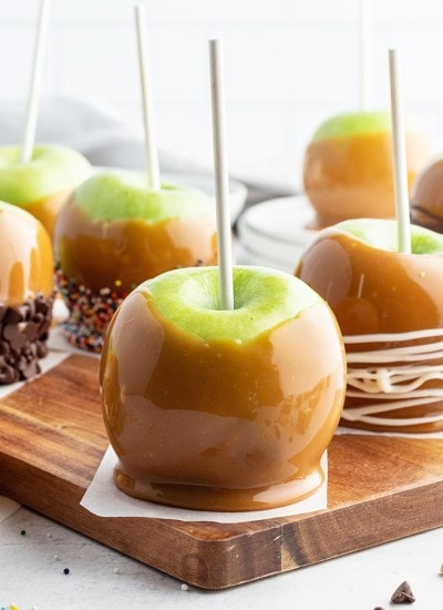 A caramel covered apple on a wooden board.