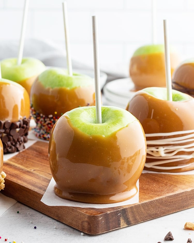 A caramel covered apple on a wooden board.