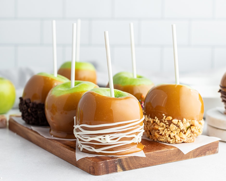 Caramel Apples on a cutting board dipped in various toppings.