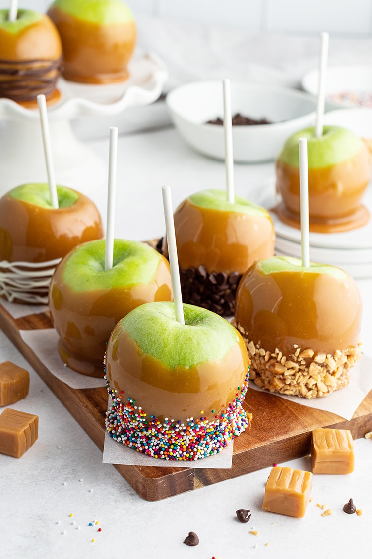 Several caramel apples dipped in various toppings like sprinkles, and peanuts, displayed in a nice spread.