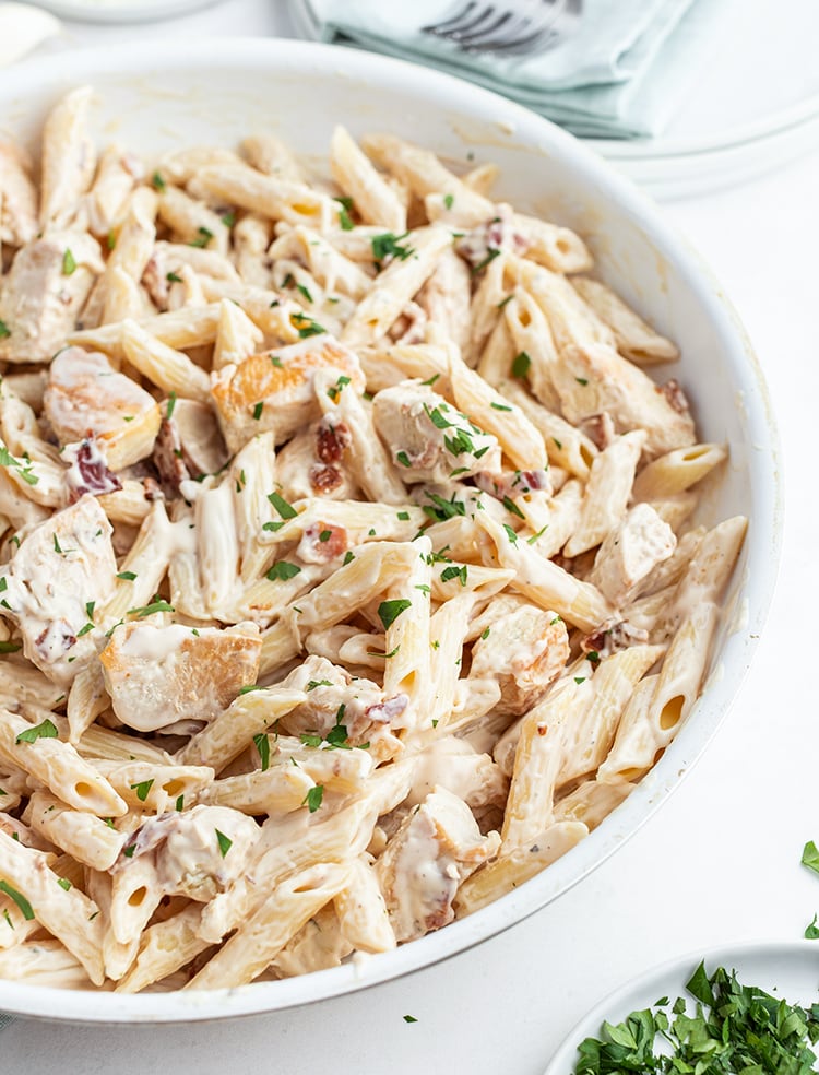 A Pasta dish in a pan with penne noodles and chicken in a white sauce. Topped with parsley.