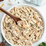 A Pasta dish in a pan with penne noodles and chicken in a white sauce. Topped with a sprinkle of parsley.