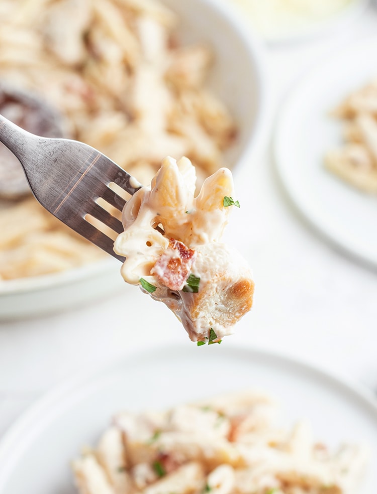 A bite of pasta on a fork showing noodles, chicken, and bacon.