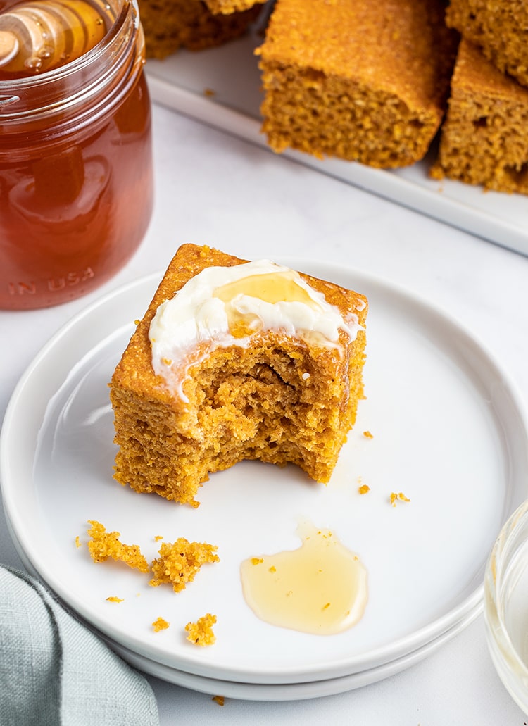 A piece of pumpkin cornbread with butter and honey on it, and a bite taken out.