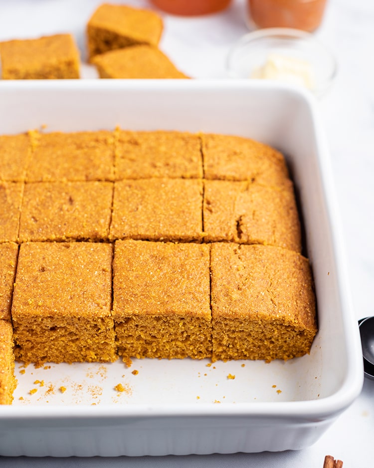 Pumpkin cornbread cut into pieces in a white baking dish