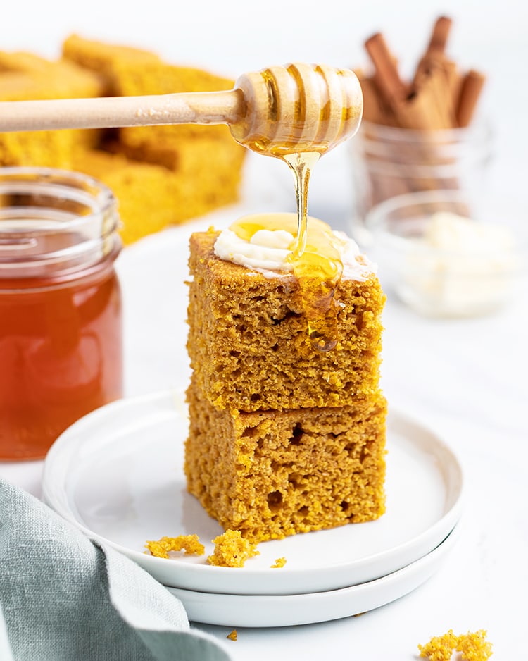 A stack of two pieces of pumpkin corn bread with butter and honey drizzled on top