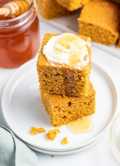 A stack of two pieces of pumpkin corn bread with butter and honey on top